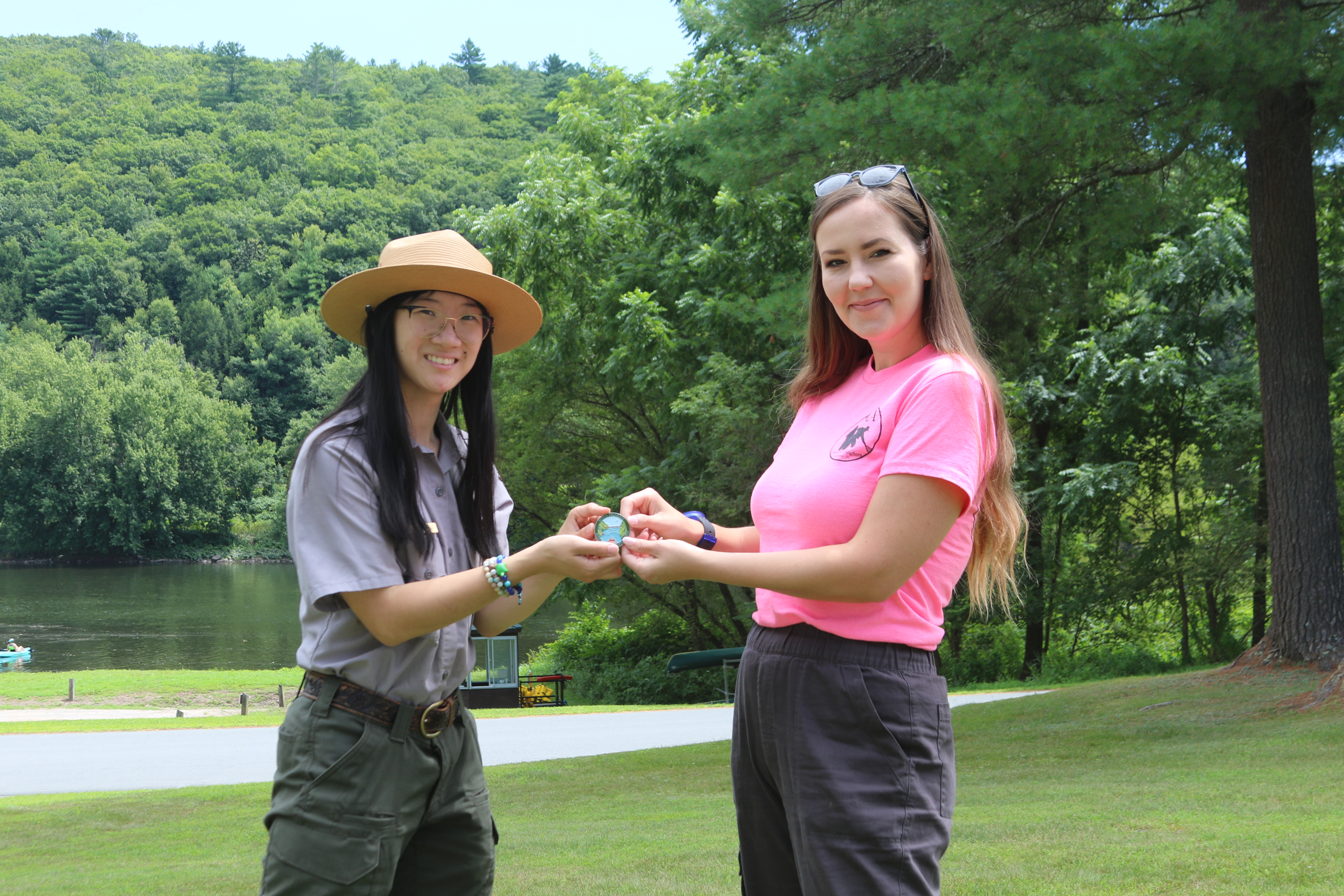 Park ranger and young woman stand together, holding small medallion together.
