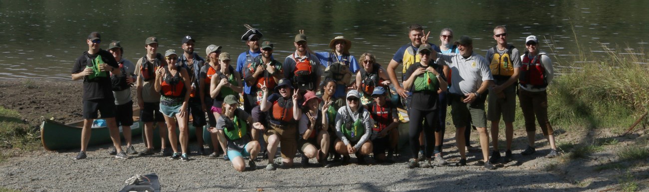 Group of 30-40 individuals in life jackets at Ten Mile River access, smiling and goofing off.