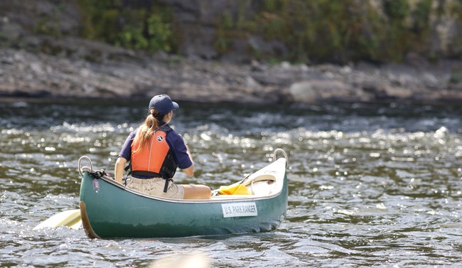 Female intern in green canoe paddling on the river.