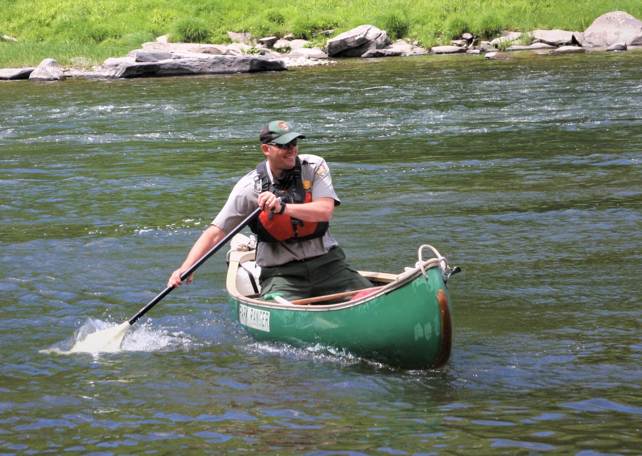 Park Ranger sitting in a green canoe paddling on the Upper Delaware River.