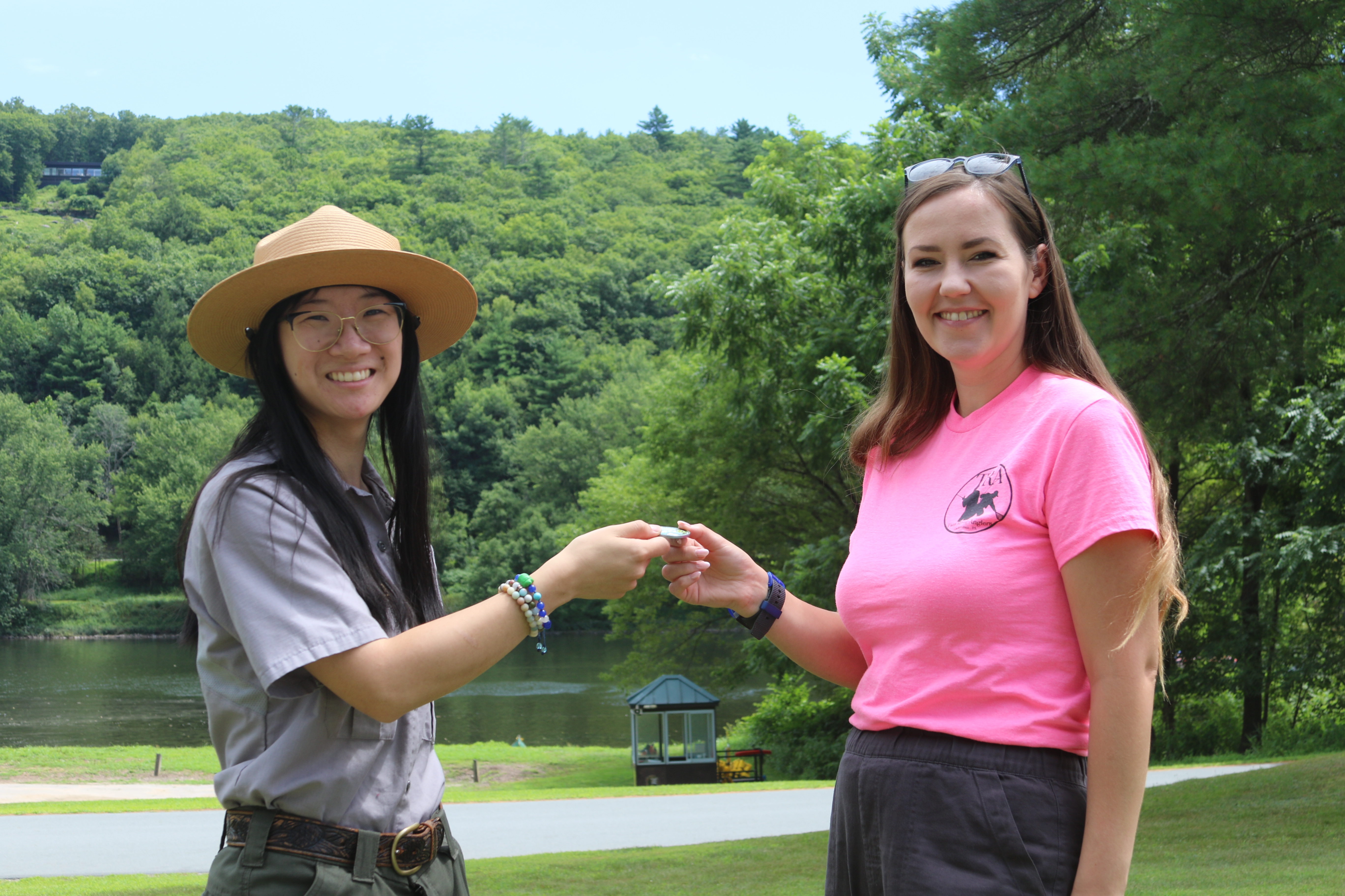 Park ranger hands a young woman a coin-like medallion, both women smile.