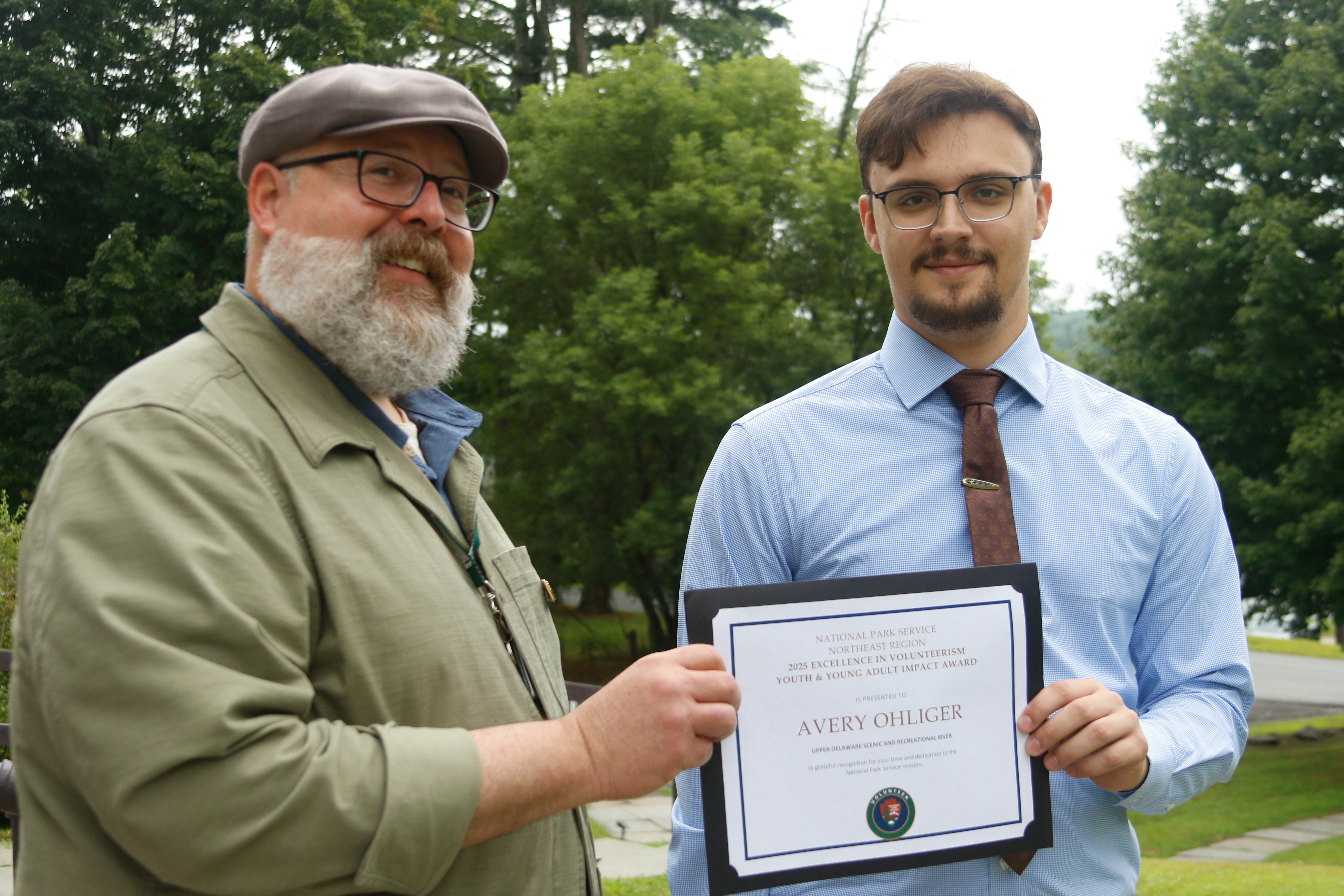 Middle-aged man hands a certificate to a younger man.