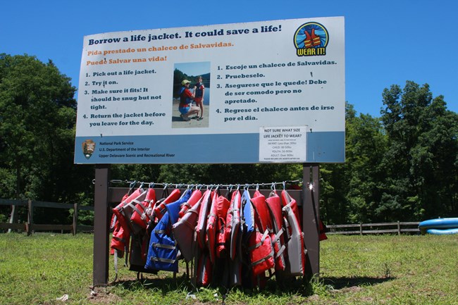 Bulletin board with line of life jackets hanging below the sign.