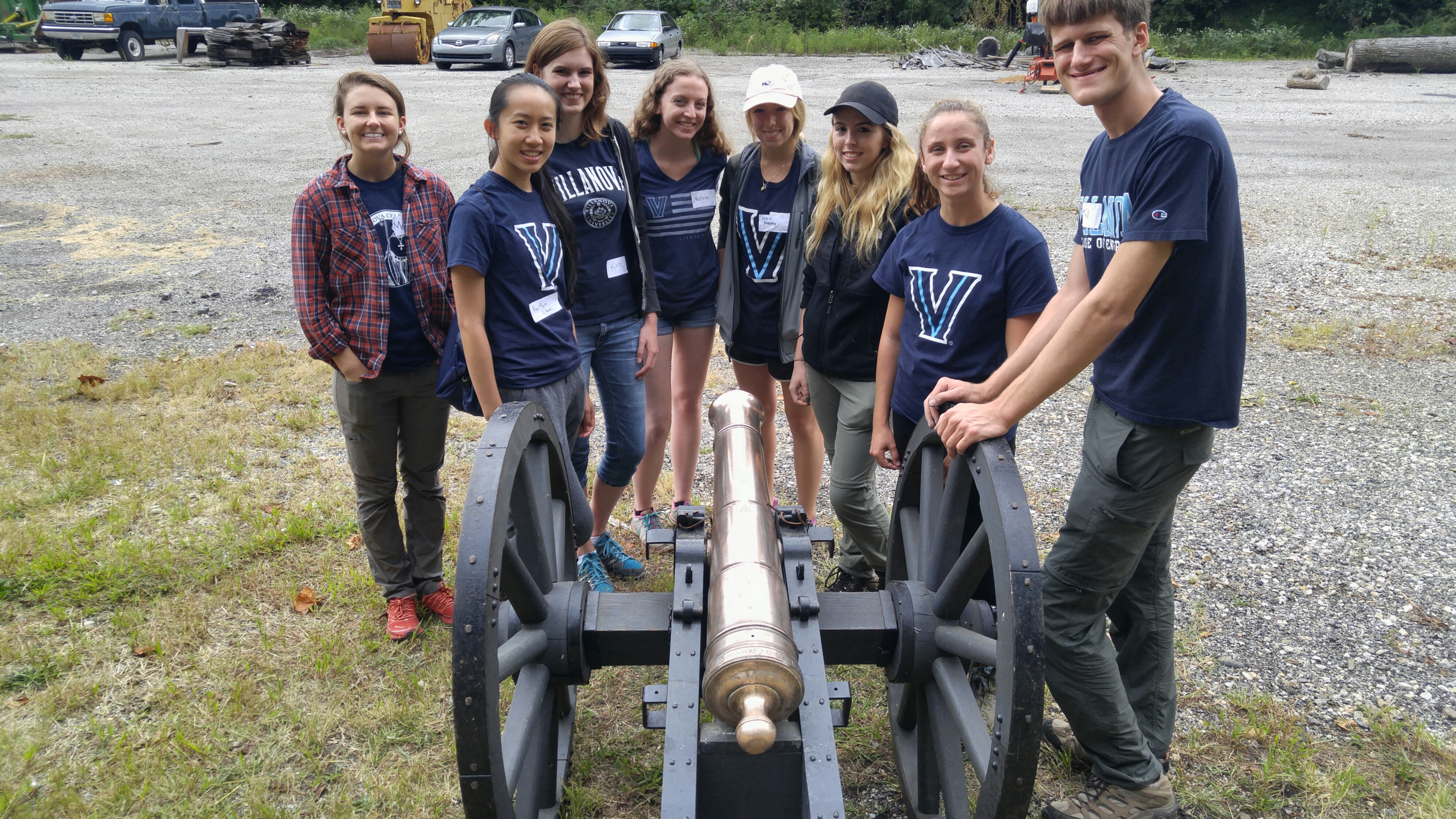 A group of college students stand around a shiny, polished cannon. A group of college students stand around a shiny, polished cannon.