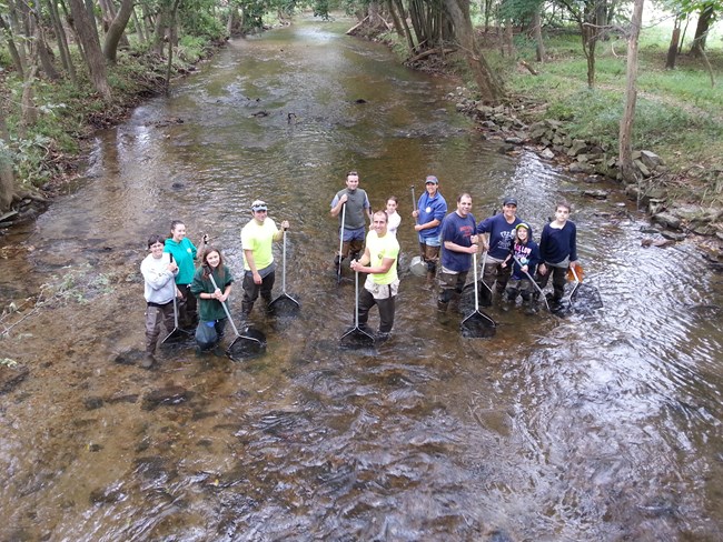 A group of people standing in a creek holding fishing nets.