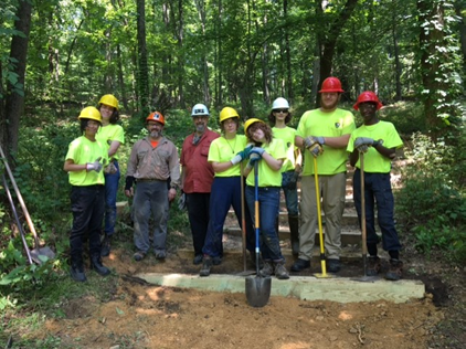 photograph, Nine smiling people wearing hard hats hold shovels and wear gloves