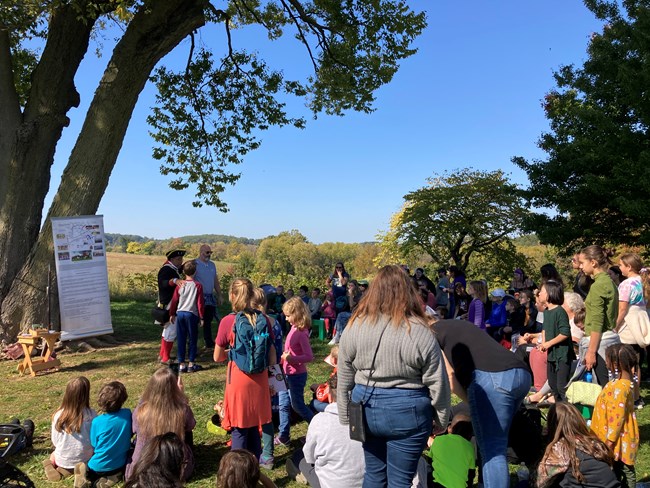 Children and adults gather around a soldier wearing a Revolutionary War soldier uniform