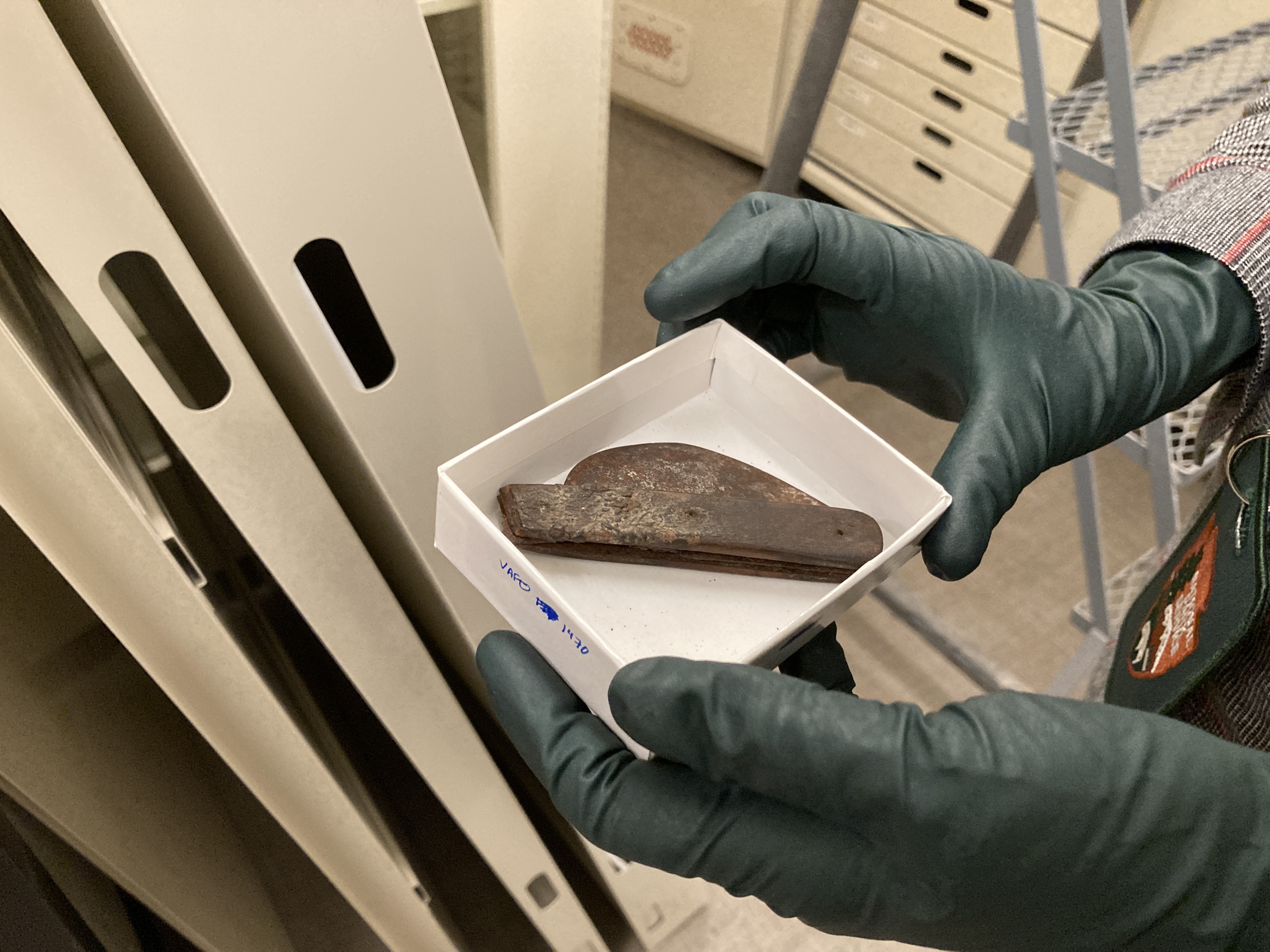 a closeup of a box held by gloved hands containing a rusty folding knife