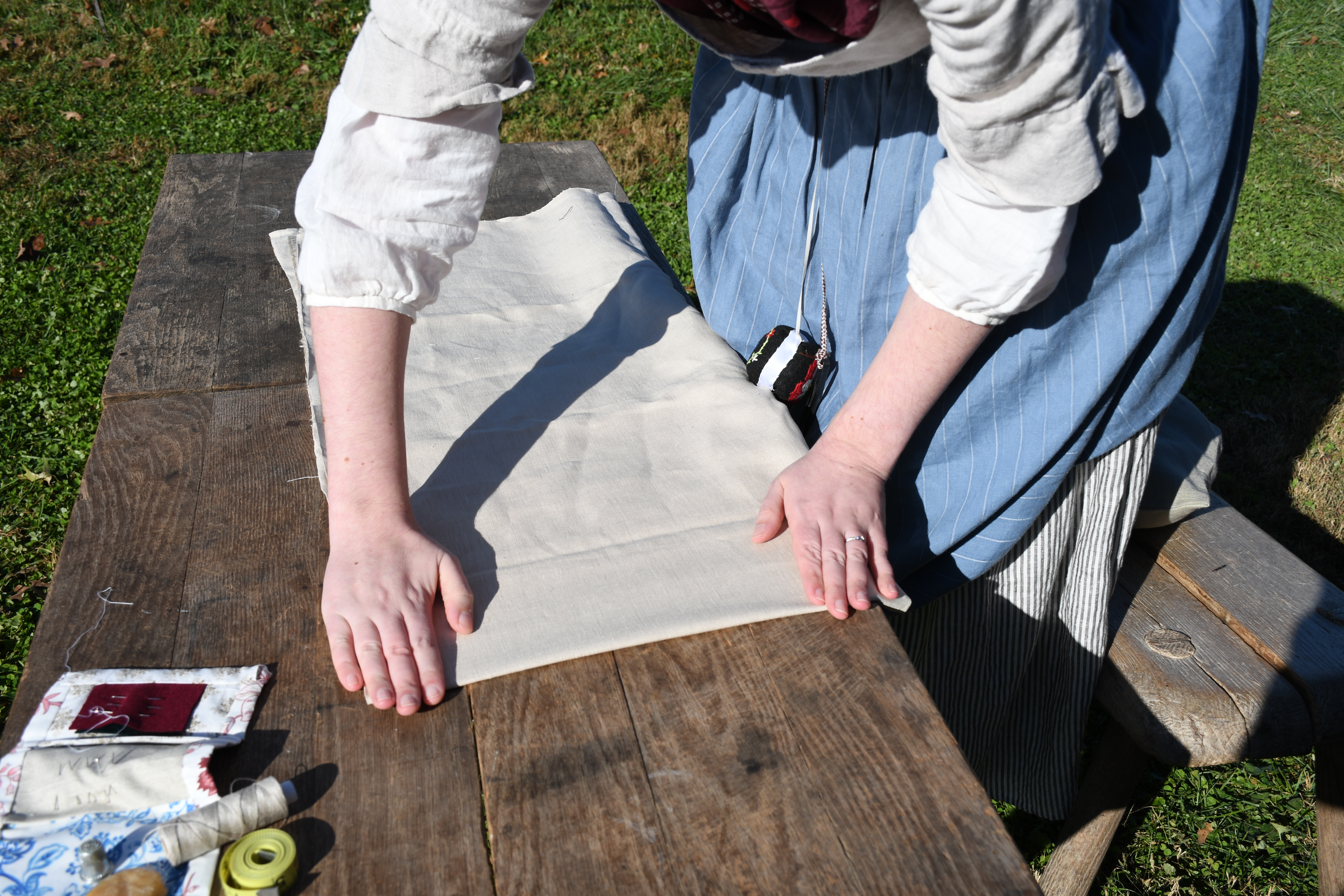 photograph, outdoors, woman folds fabric in half and presses seam with both hands.