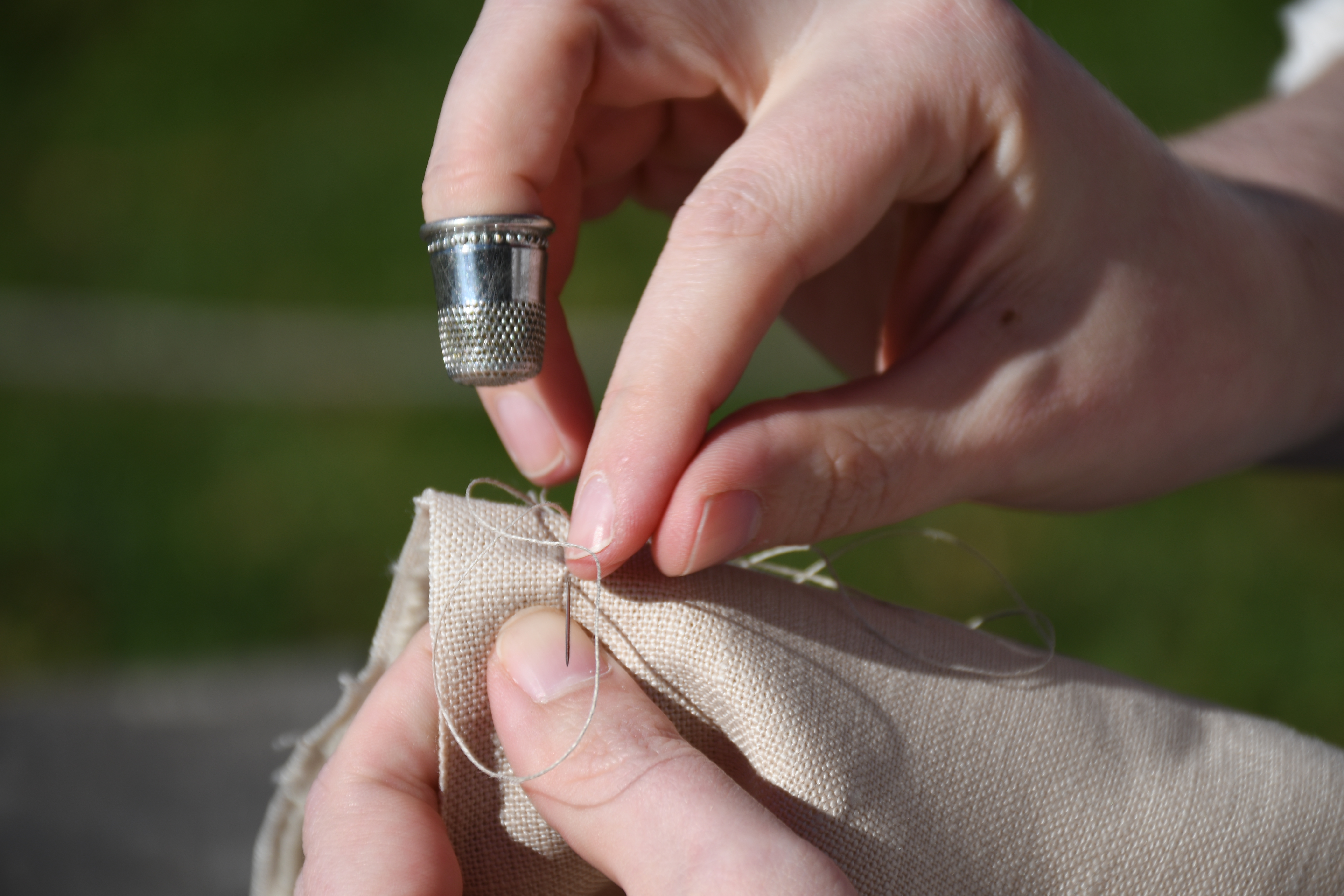 photograph, outdoors, closeup of woman's hand pulling needling through fabric