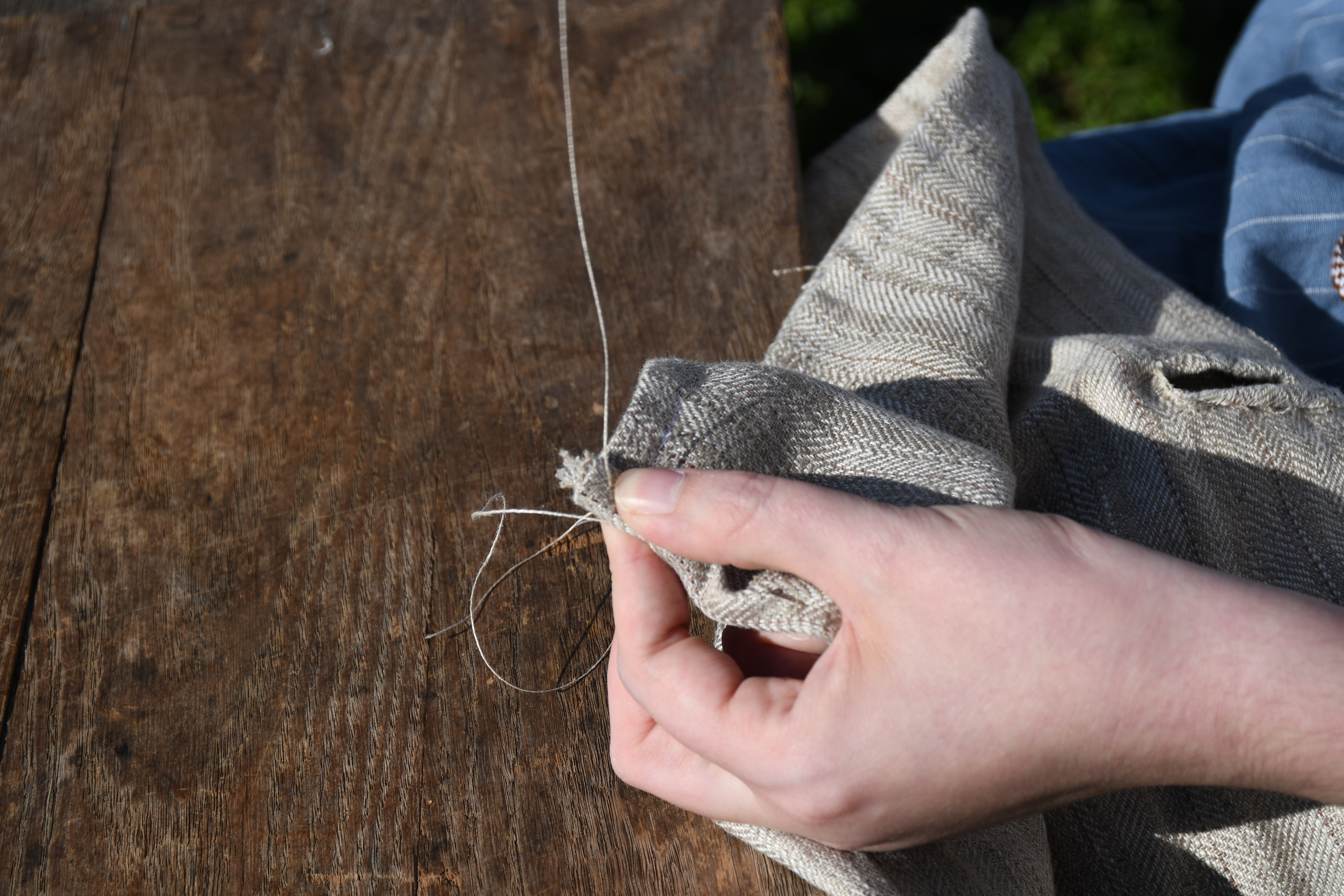 photograph, outdoors, closeup of woman's hands making a whipstitch on an end seam