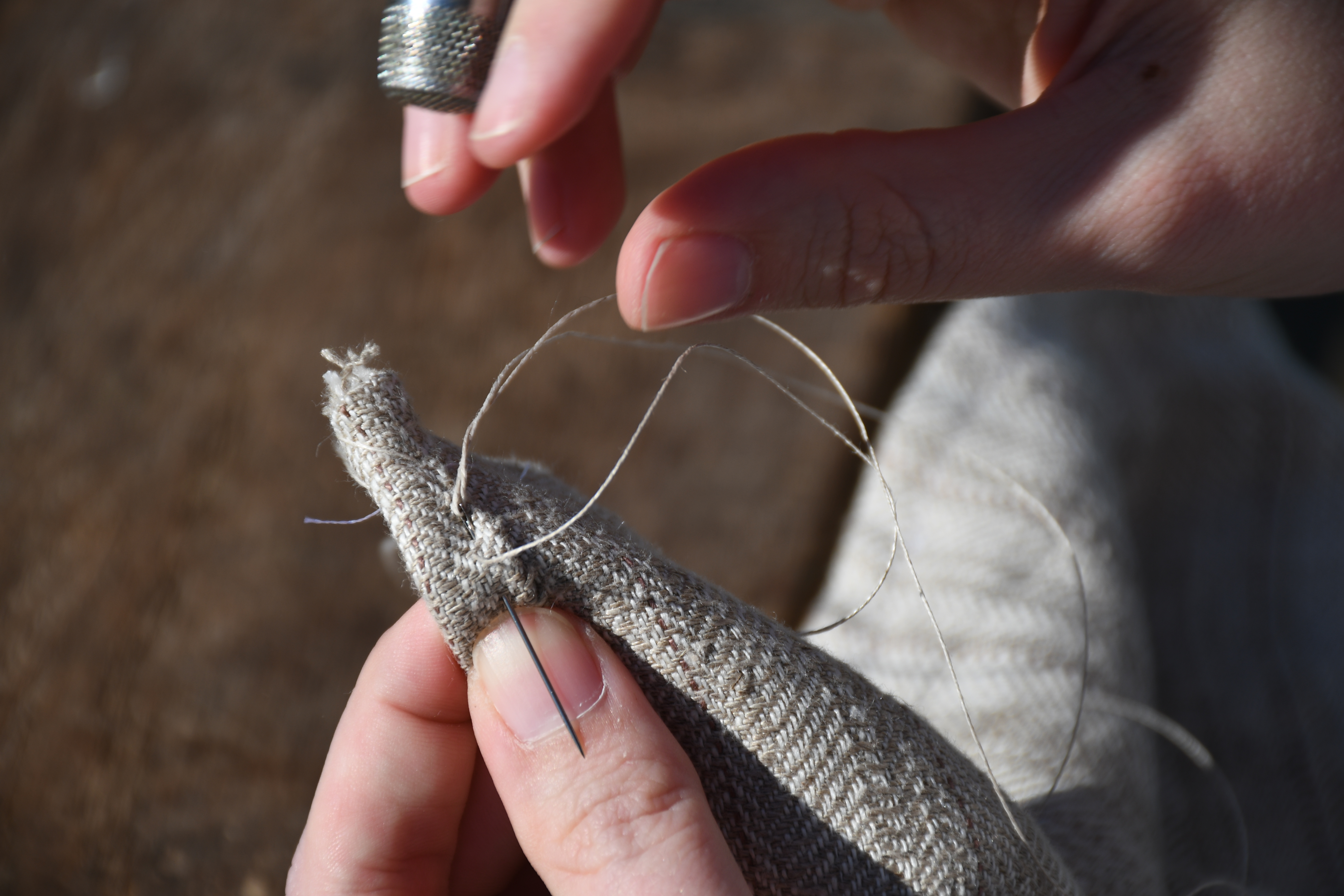 photograph, outdoors, closeup of woman's hands pulling thread to finish a whipstitch on an end seam interior hem