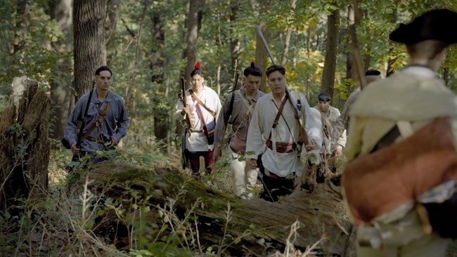 Oneida men walk through a forest towards a Continental soldier with his back to the camera.