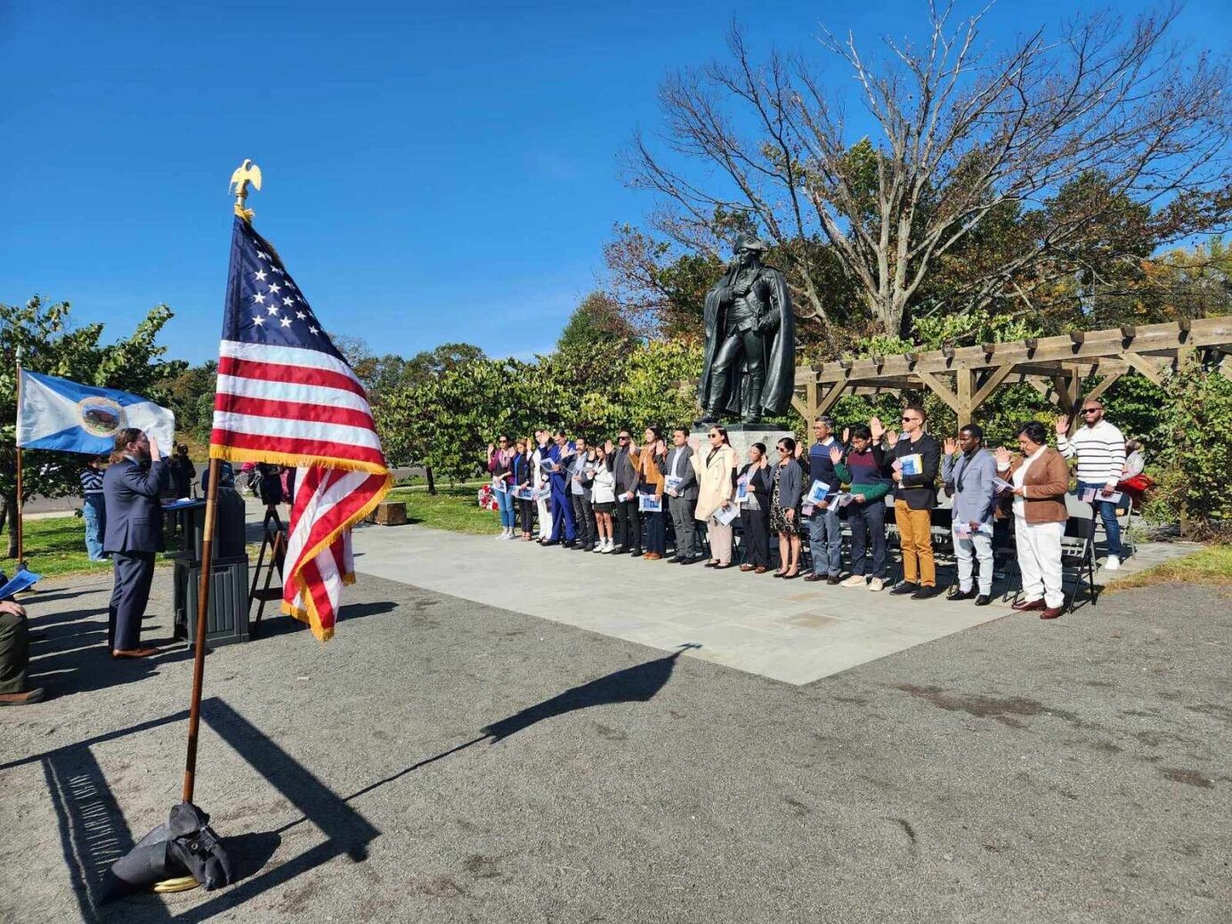 Twenty new American citizens take their oath in front of a statue of General von Steuben
