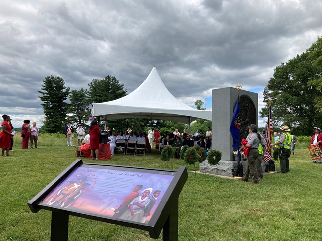 A brightly colored wayside exhibit panel in front of the Patriots of African Descent Monument