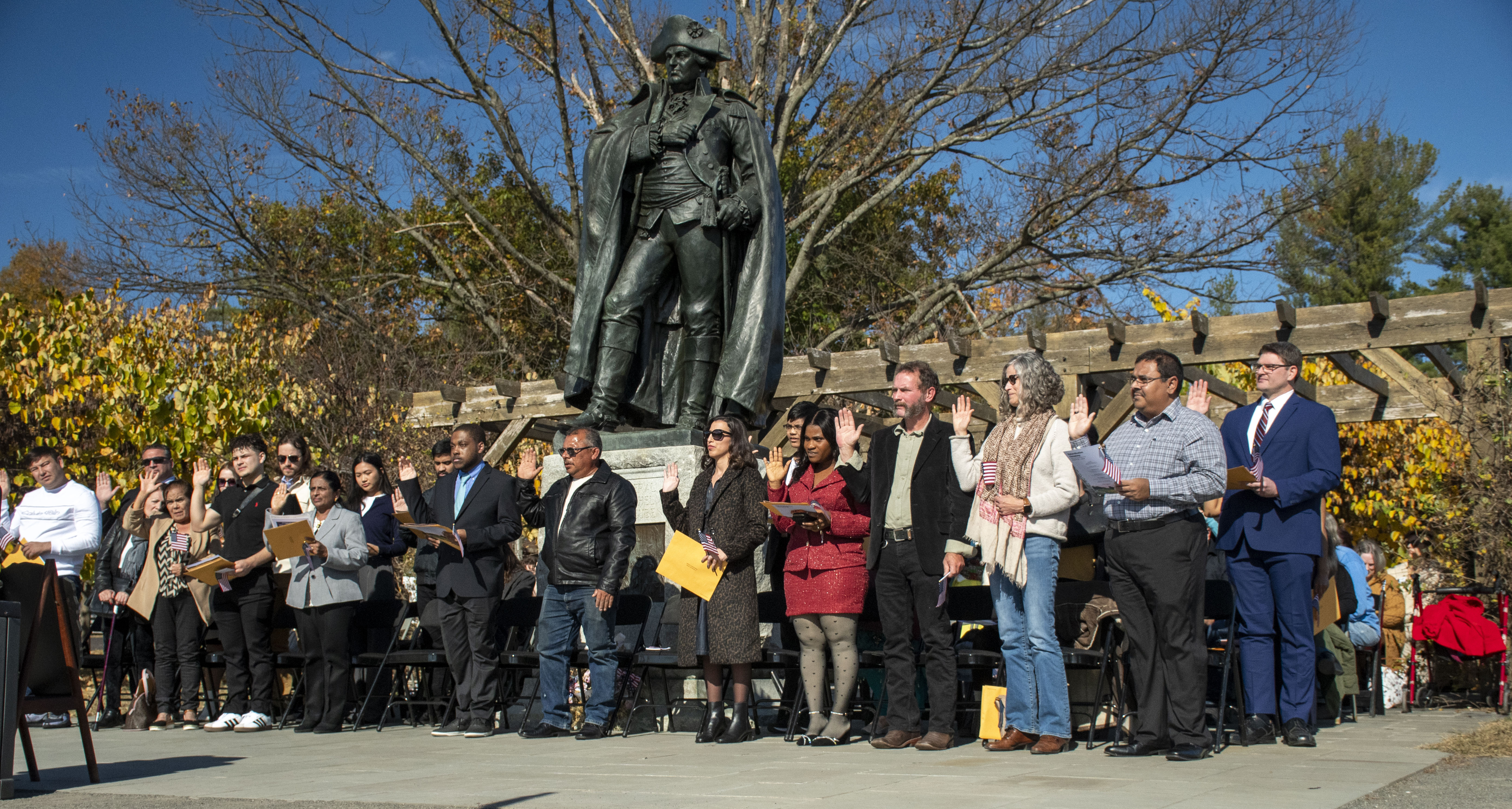 Naturalization Ceremony 2024 A group of people with their right hand raised are standing among a tall statue.
