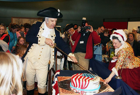 George Washington cuts a birthday cake while Martha Washington watches.