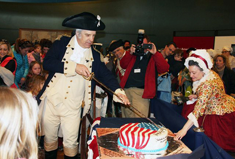 George Washington cuts a birthday cake while Martha Washington watches.