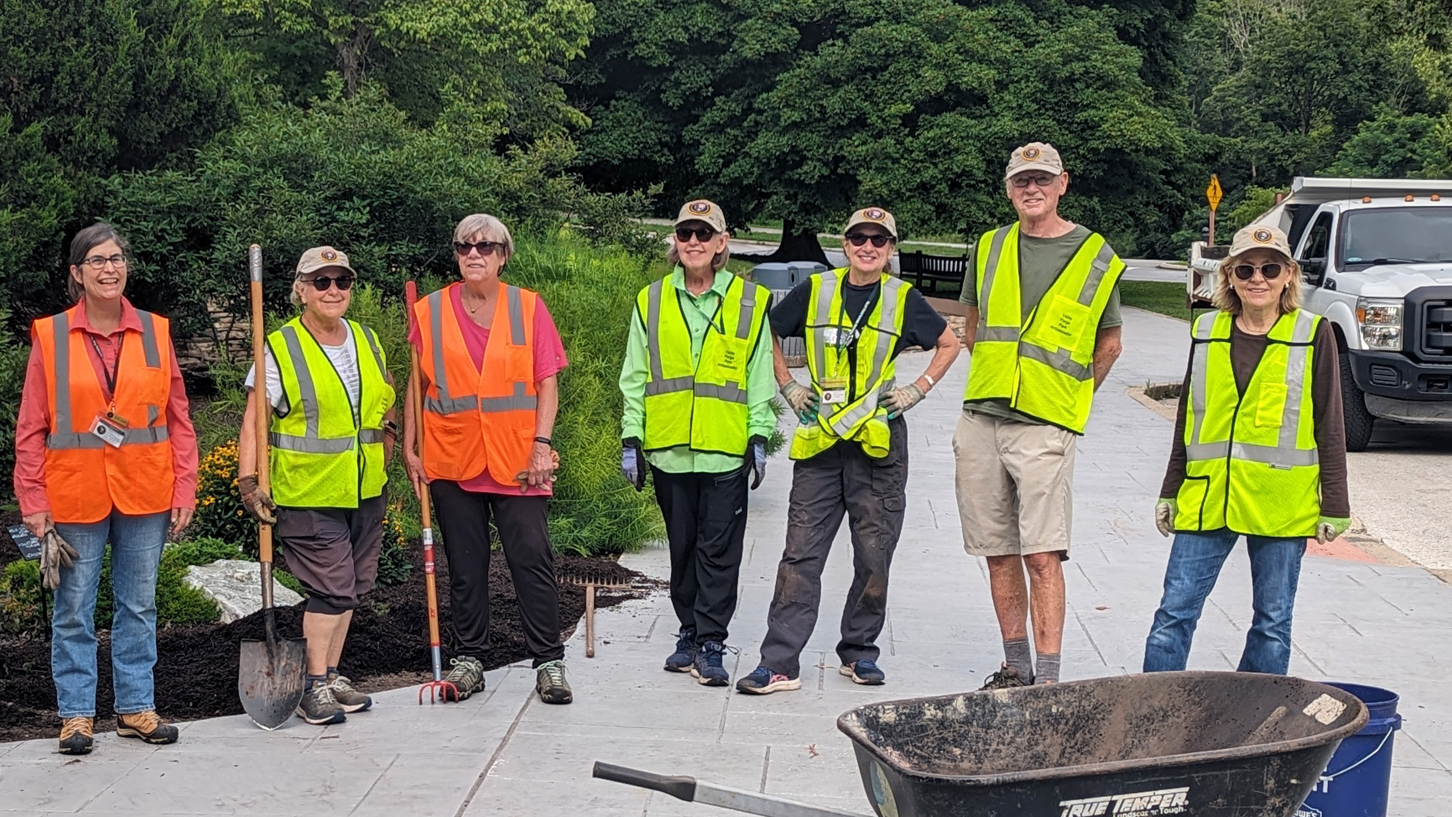 Seven smiling people stand holding tools and wearing high-visibility work vests.