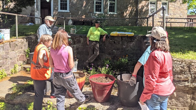 Six people stand near large pots for plants.