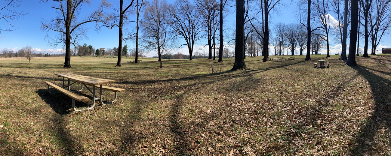 a wooden picnic table sits in the shade of trees and the national memorial arch is visible in the distance