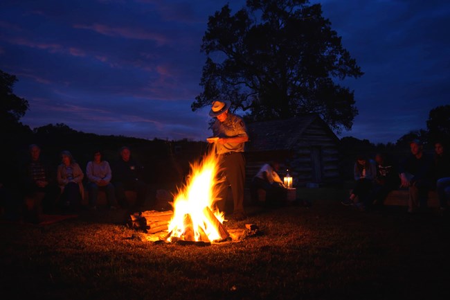 a ranger stands by a glowing fire after dark