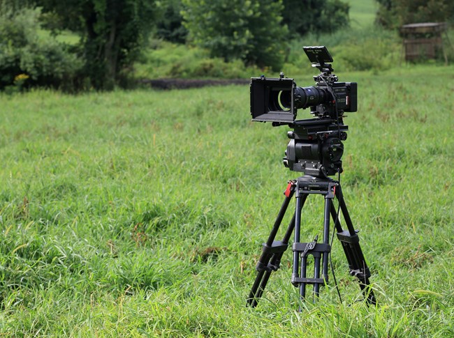 A camera with a large lens on a tripod in a grassy field.