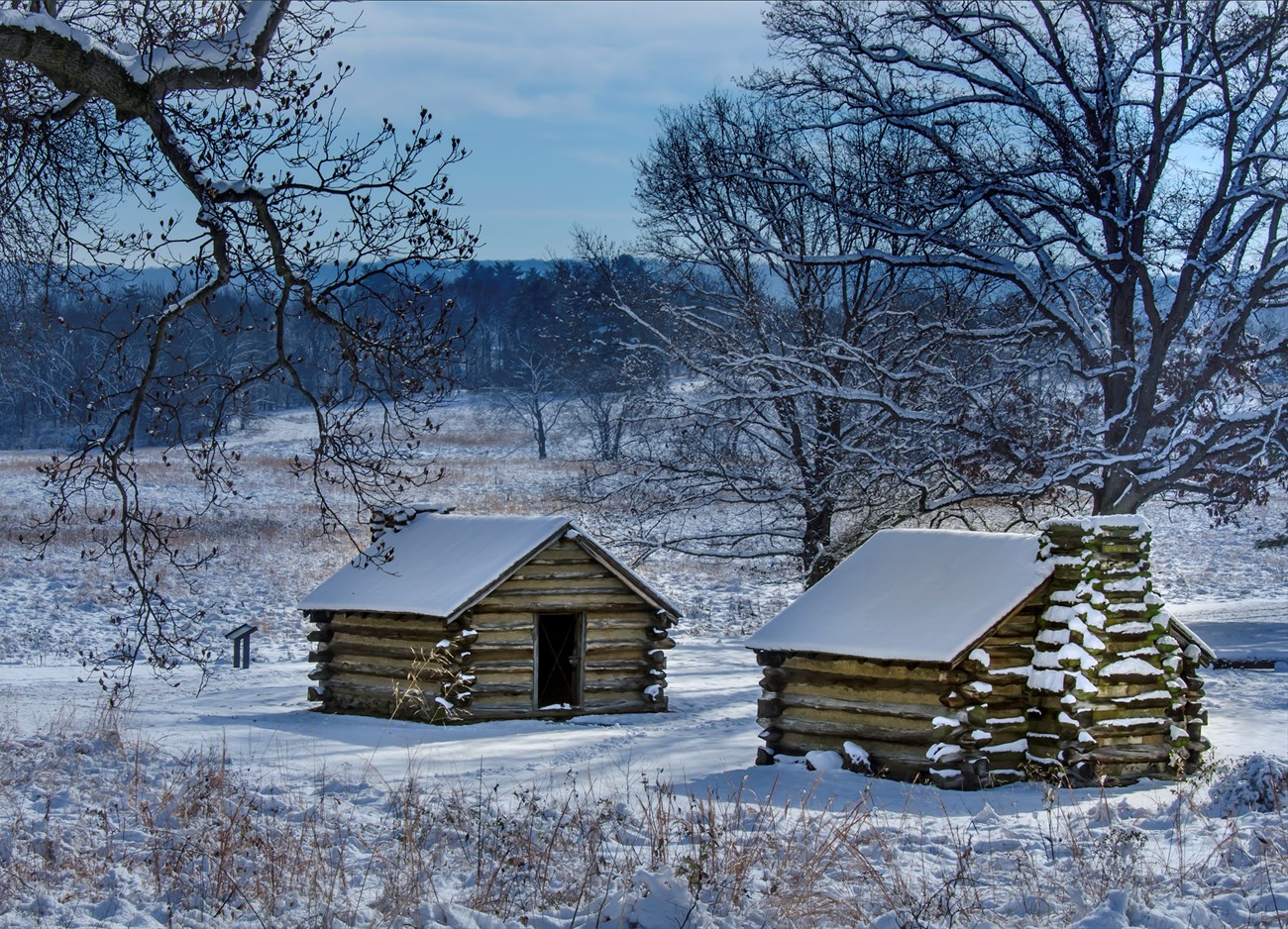 two log huts and a snow covered landscape