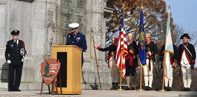 Men in military uniforms stand with flags under the National Memorial Arch