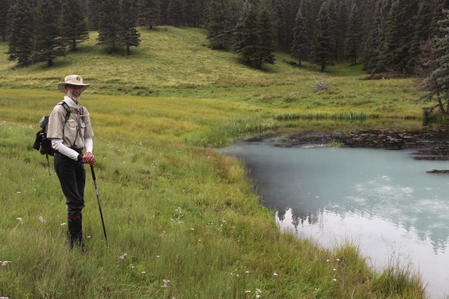A park volunteer stands beside a geothermal pond and smiles at us.