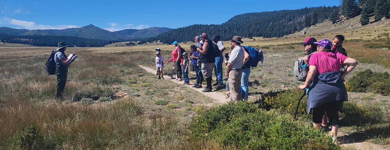 A park ranger addresses a group of students and chaperones on a hiking trail.