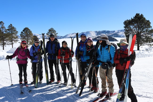 A group of cross-country skiers pauses for a photo in a snowy valley.