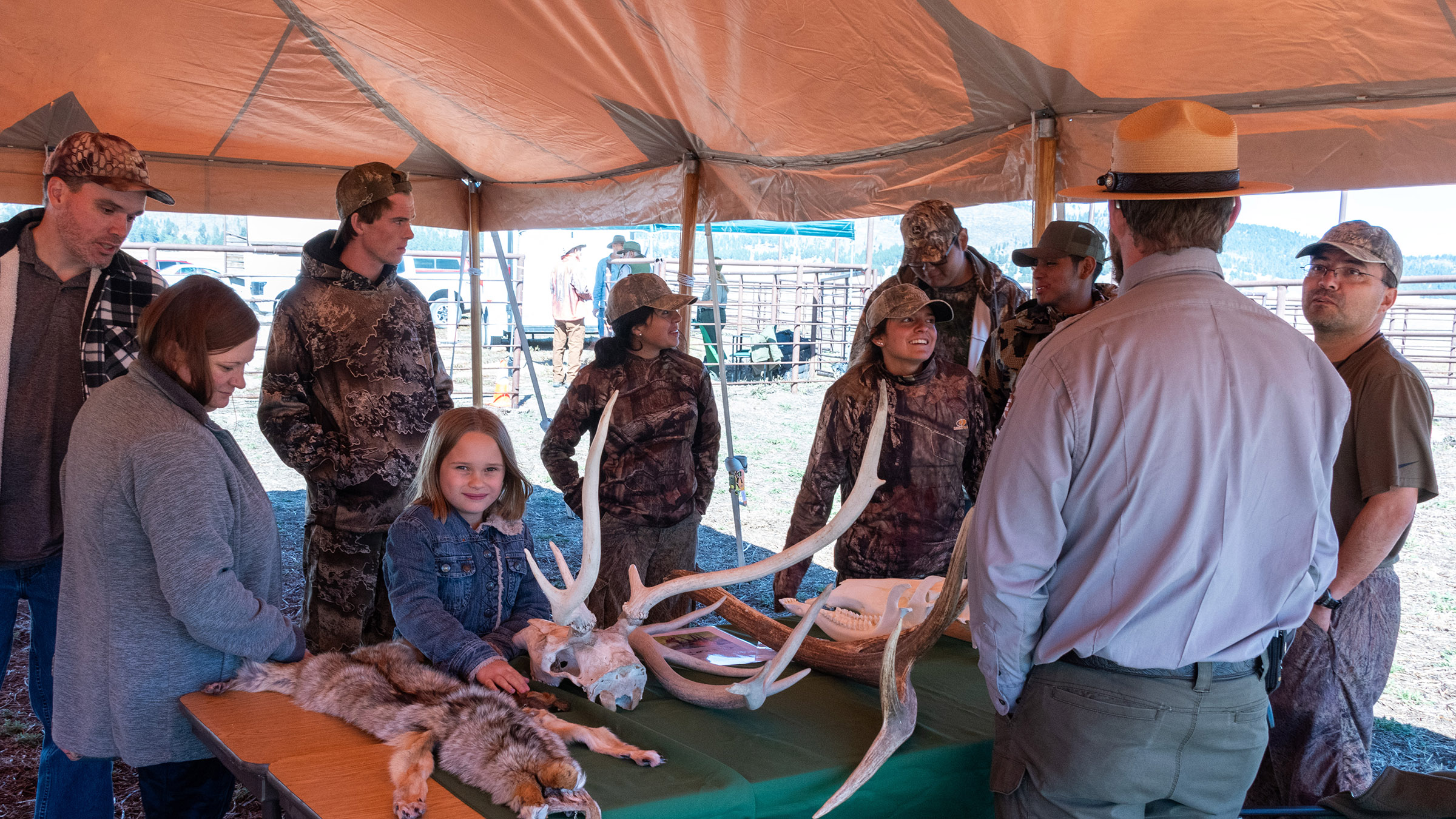 Fall Fiesta 2023 visitors talking with a ranger about wildlife. Visitors stand at a table covered with pelts and skulls to talk about wildlife with a ranger.