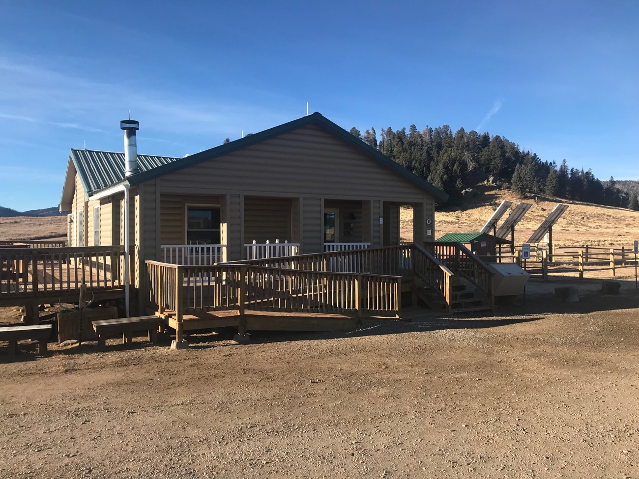 Entrance Station at the base of Cerro La Jara Small tan building with a wooden ramp and steps standing in front of a gravel parking lot.