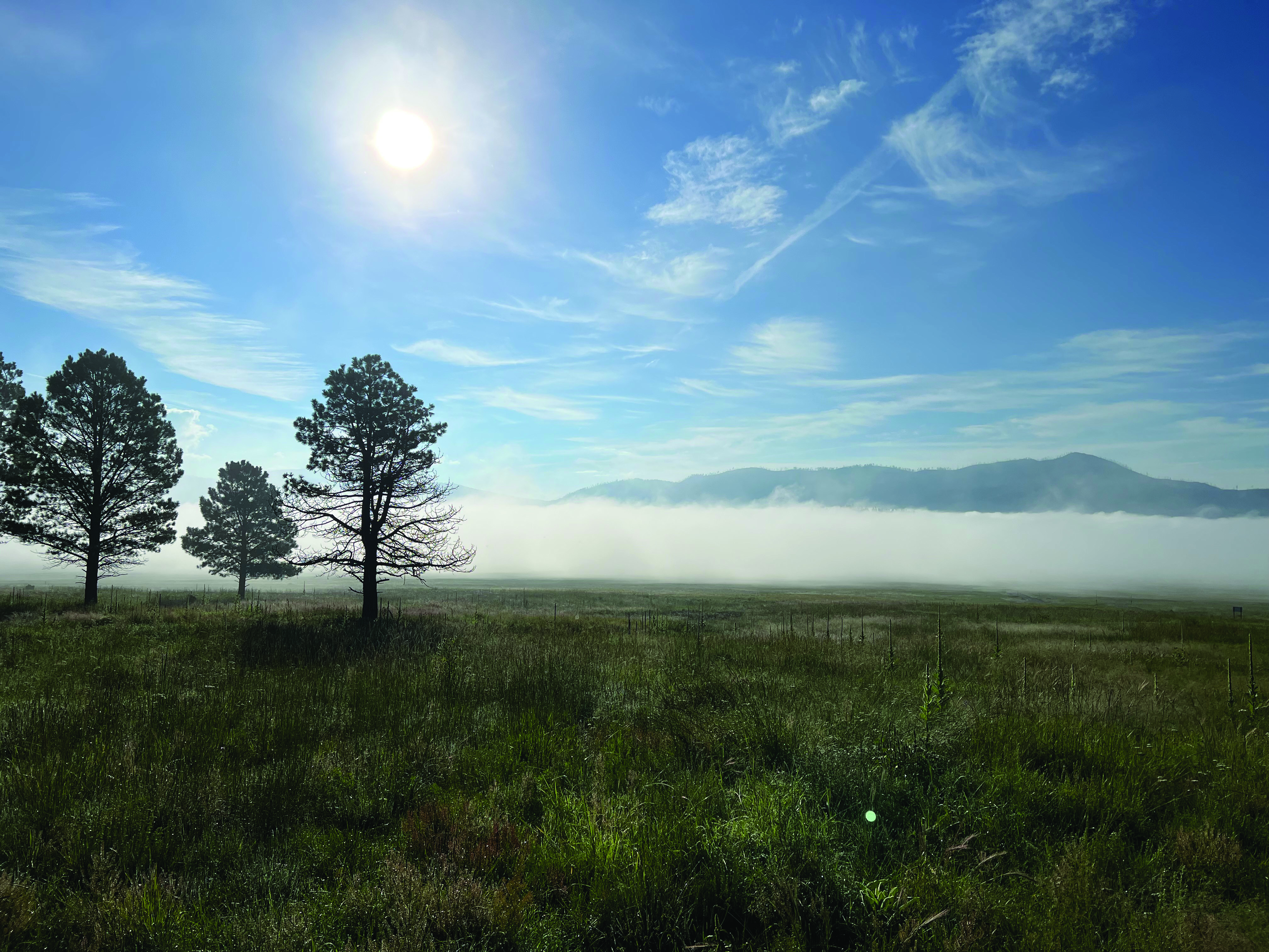 Fog fills a large alpine valley with mountains barely visible.