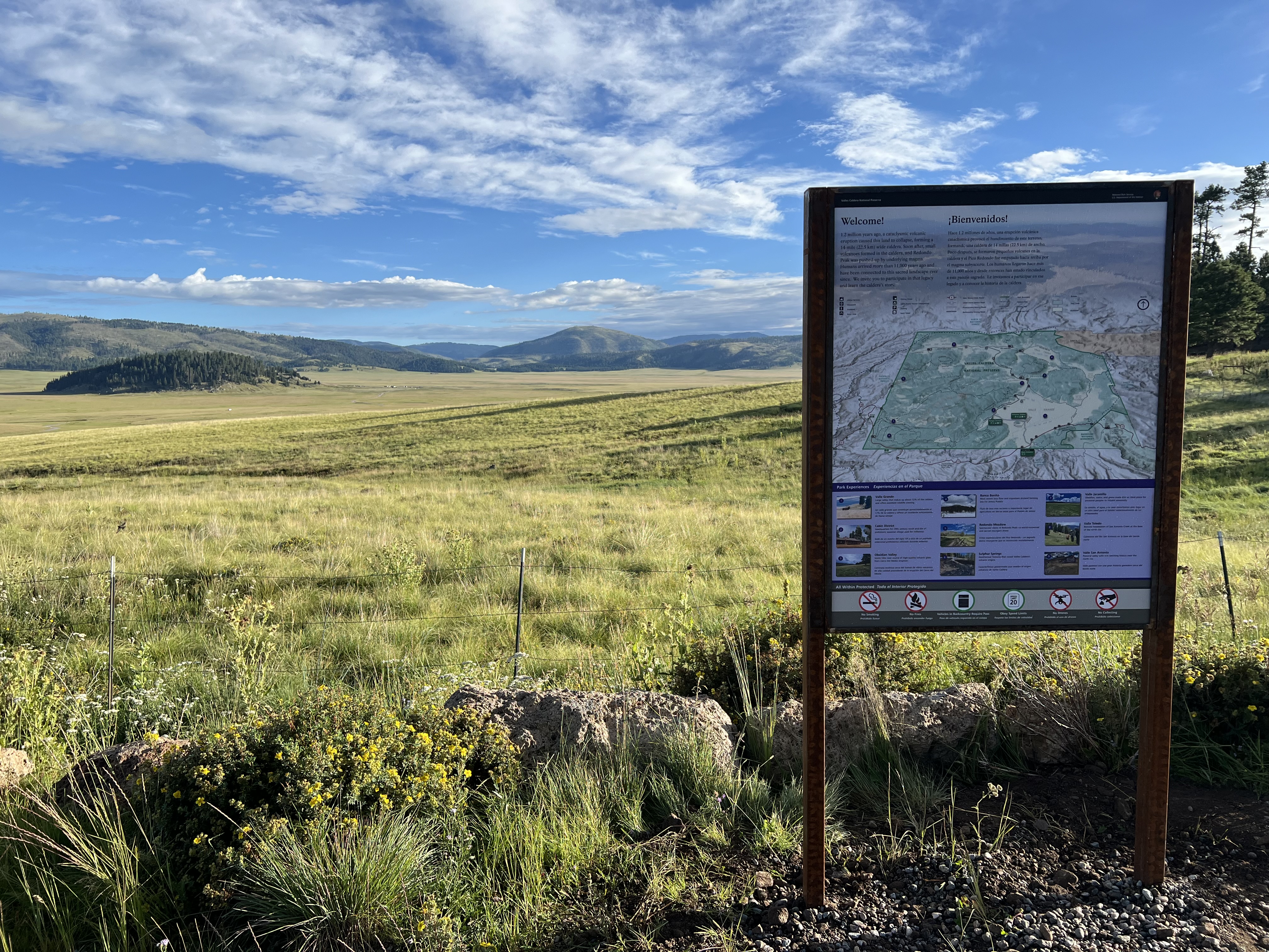 Orientation sign with the map of the park stands in front of an expansive view of a large alpine valley.