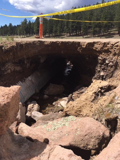 A section of road blocked off showing the washed out culvert underneath.
