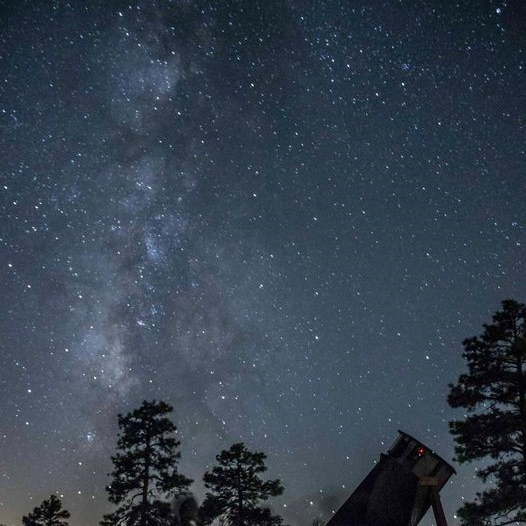 A telescope points toward a starry night sky.