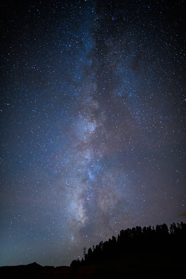 The Milky Way galaxy rises vertically above the dark silhouettes of mountains.