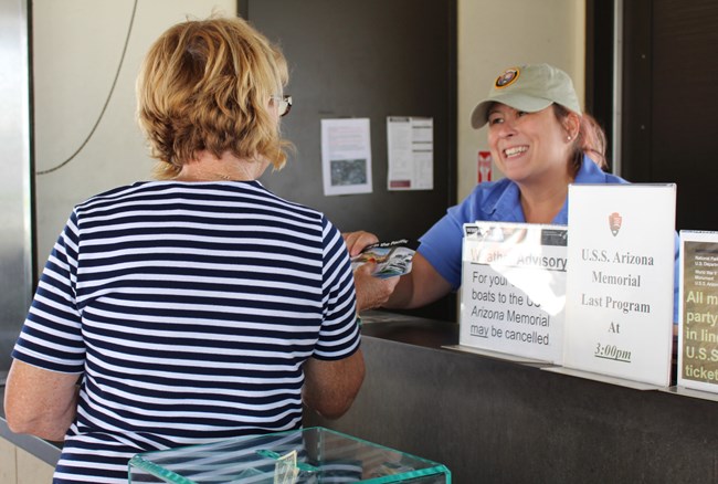 Two older women are speaking at a counter. One woman is wearing a volunteer uniform.