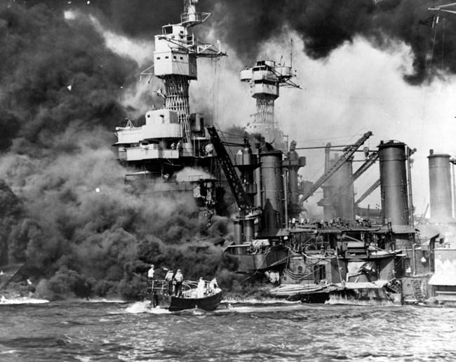 A motor launch approaches the sunken and burning West Virginia.