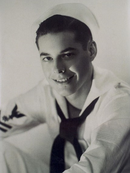 A black and white photo of a USS Arizona survivor, depicting a portrait of a veteran from World War II, wearing a military uniform with a dark tie and white cap.