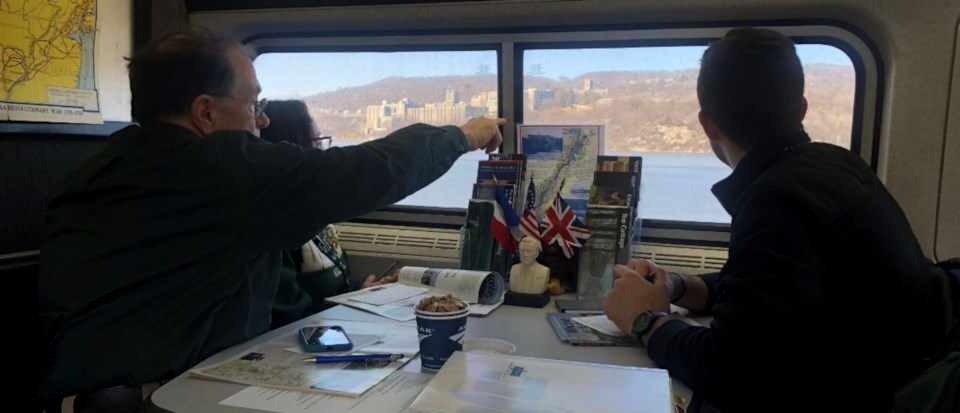 A man points to a river landscape from inside of a train car.