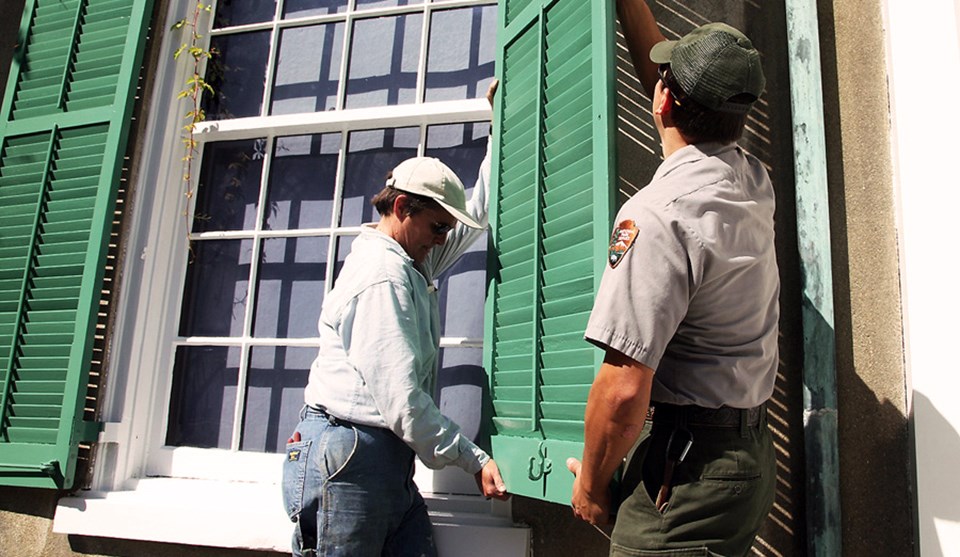 A man and woman remove a shutter from a window.