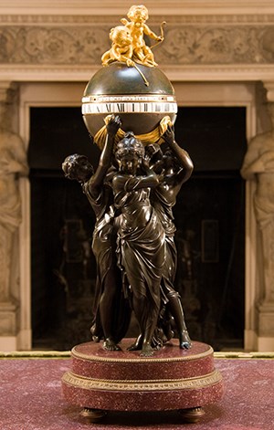 Three bronze female figures support an orb with gilt cherubs on top.
