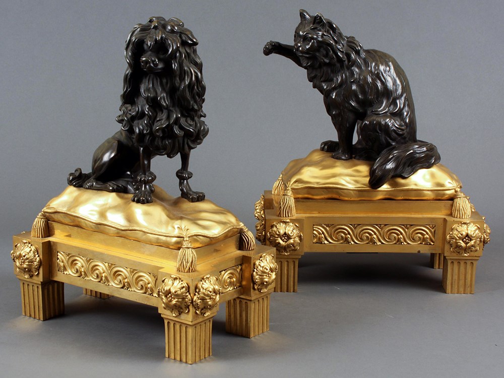 A pair of fireplace andirons, each representing a dog and a cat resting on a gilded pillow.