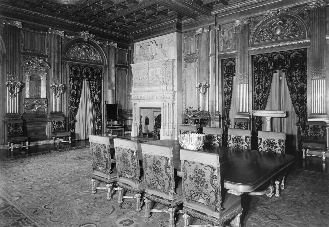A grand dining room with large carpet, table, and stone fireplaces.