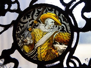 A stained glass window with image of a man wearing a large hat