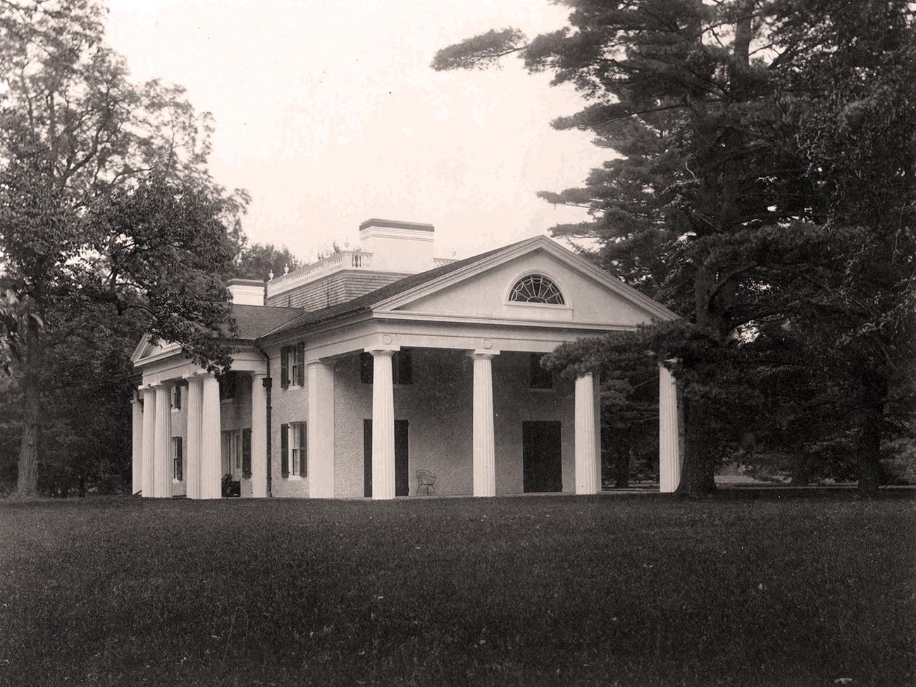 A classical building with central pedimented portico and captain's walk on the roof.