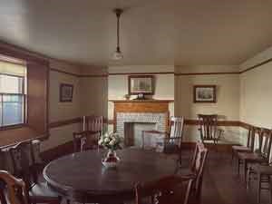 A room furnished with a round table and many chairs in front of a fireplace.